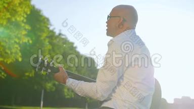 一个秃顶的人在公园里弹<strong>吉他</strong>唱歌。 <strong>吉他</strong>手触摸<strong>吉他</strong>弦。 中弹。